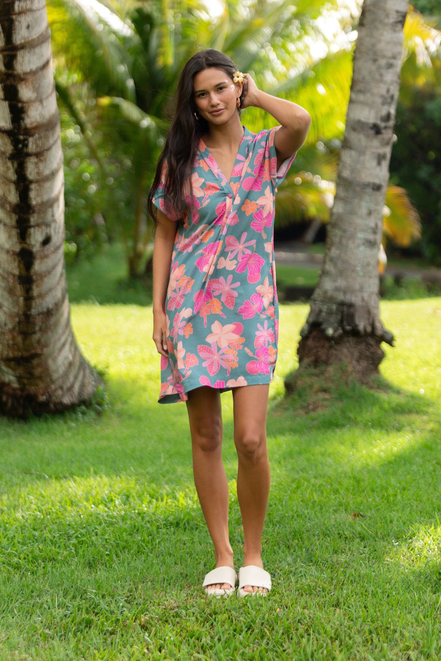 woman with brown hair wearing a teal v neck mini dress with orange and pink foral print
