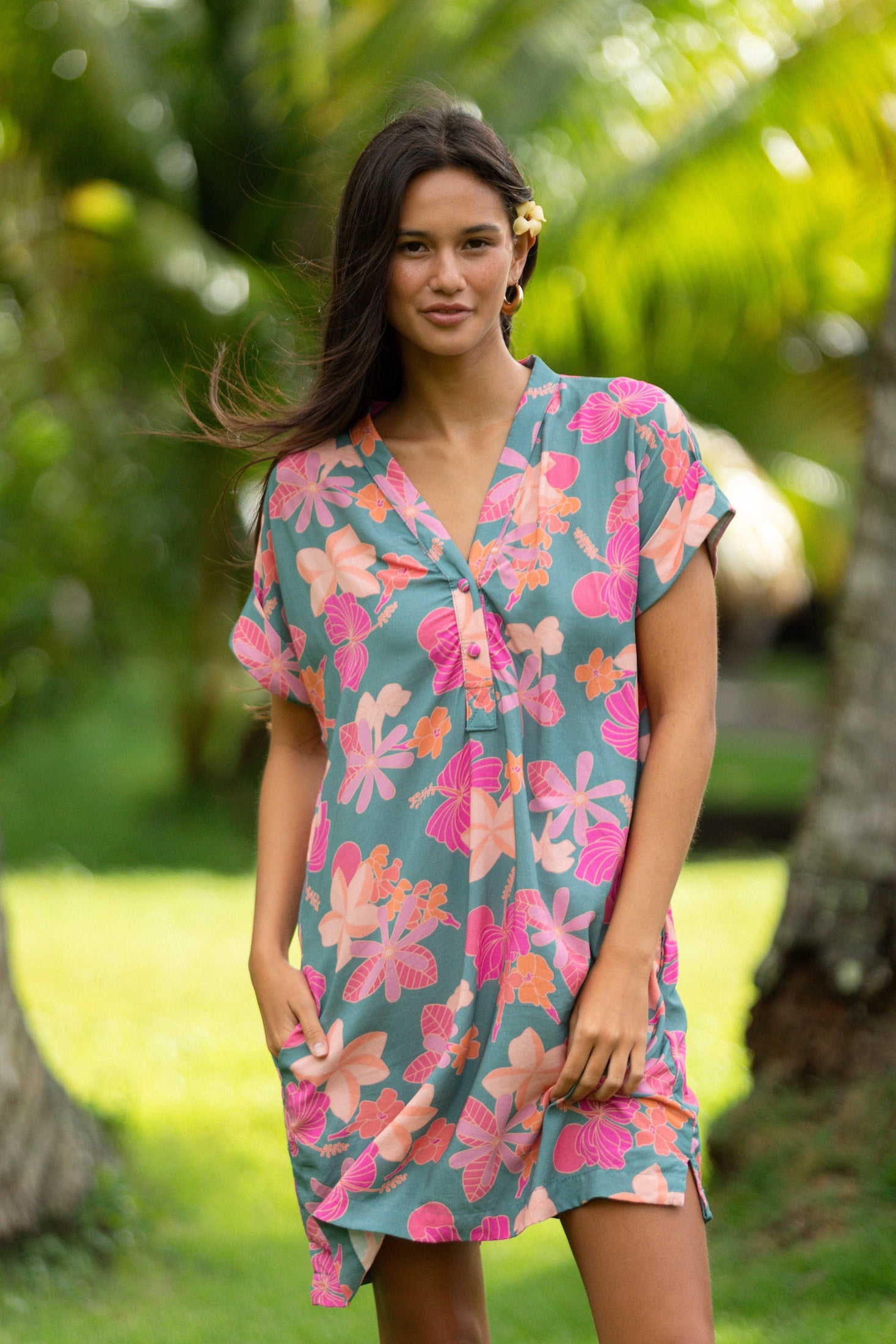 woman with brown hair wearing a teal v neck mini dress with orange and pink foral print