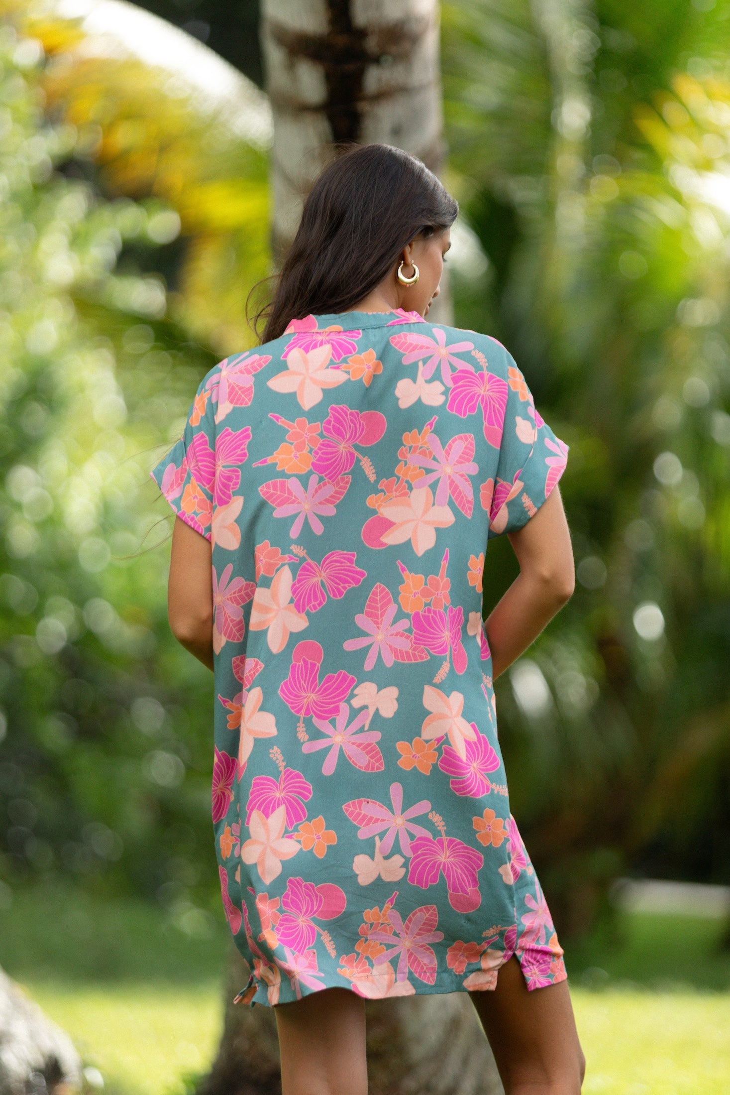 woman with brown hair wearing a teal v neck mini dress with orange and pink foral print