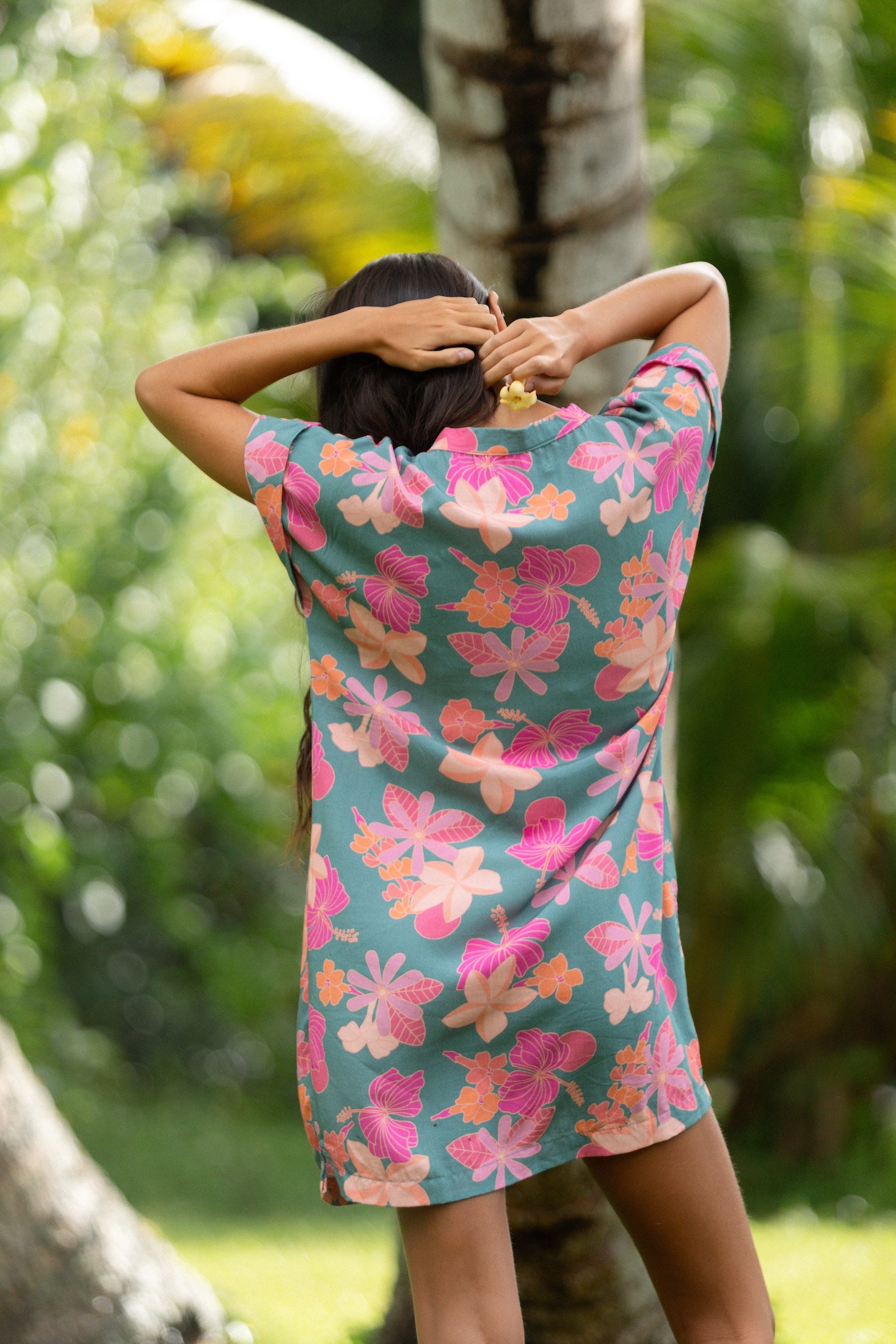 woman with brown hair wearing a teal v neck mini dress with orange and pink foral print
