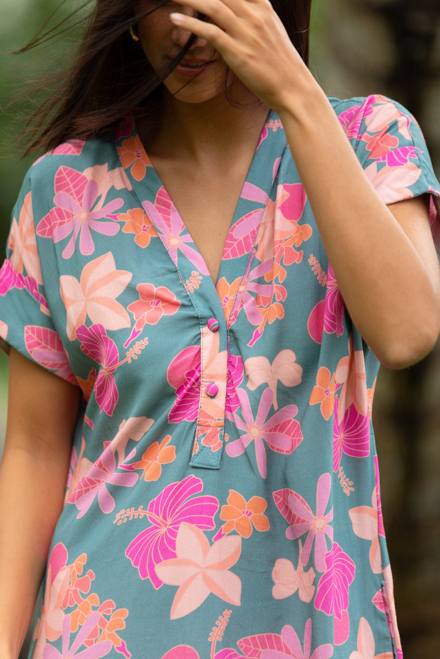 woman with brown hair wearing a teal v neck mini dress with orange and pink foral print