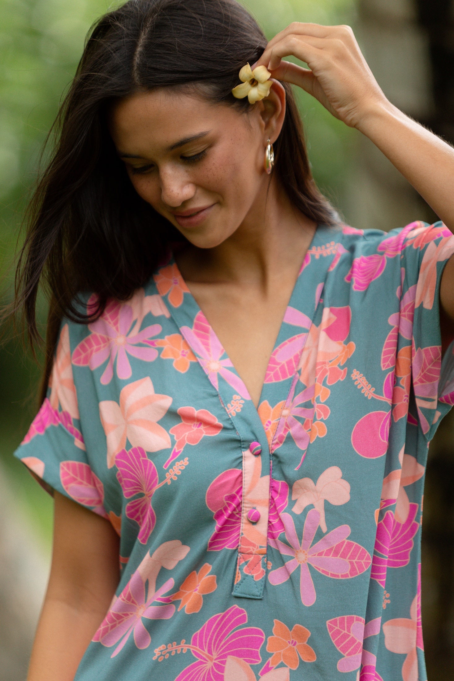 woman with brown hair wearing a teal v neck mini dress with orange and pink foral print