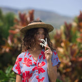 woman with brown hair wearing a mid length shirt dress with periwinkle background and bright red hibiscus print.