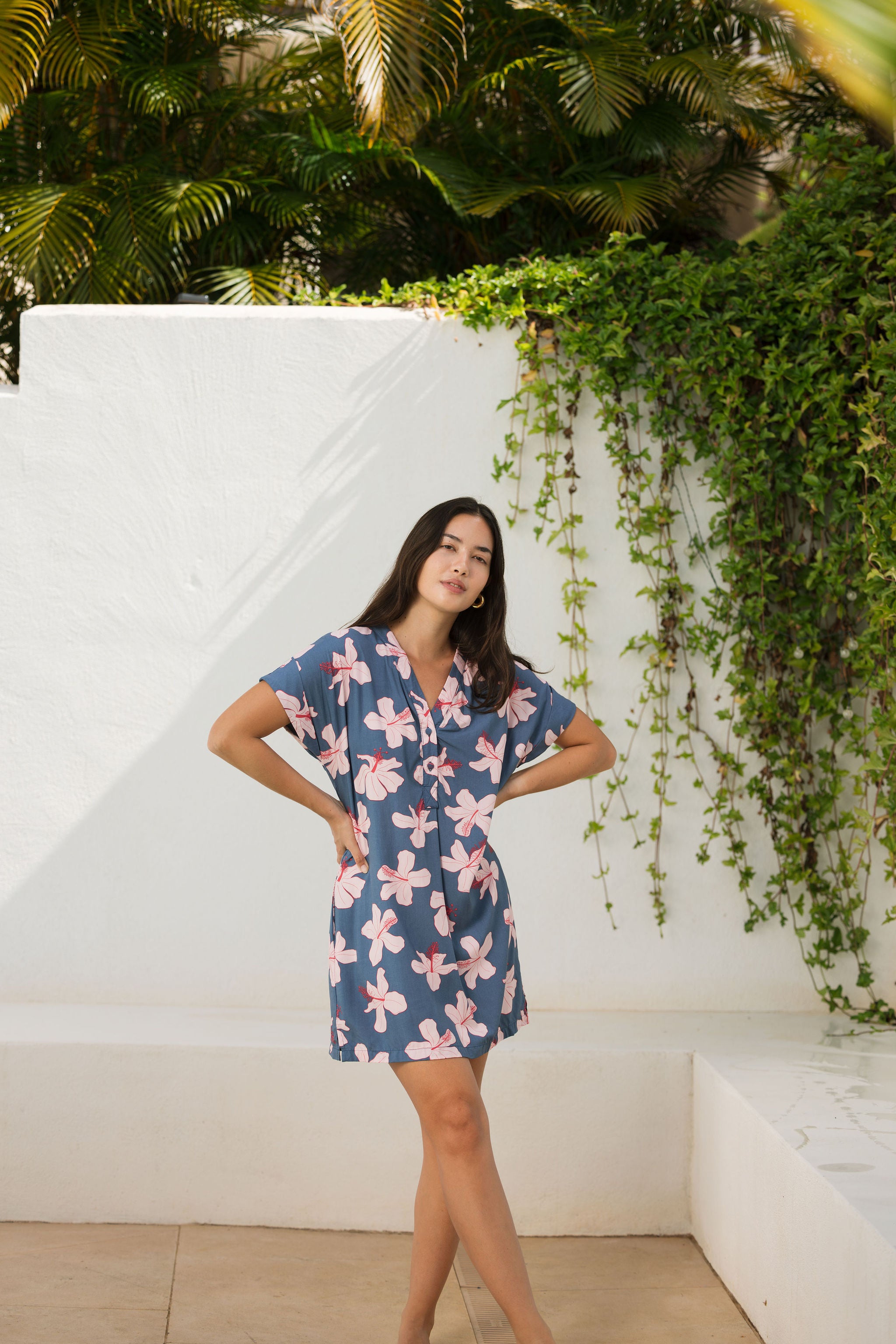 woman with black hair wearing a casual shirt dress with button up v neckline in a navy and pink hibiscus print.