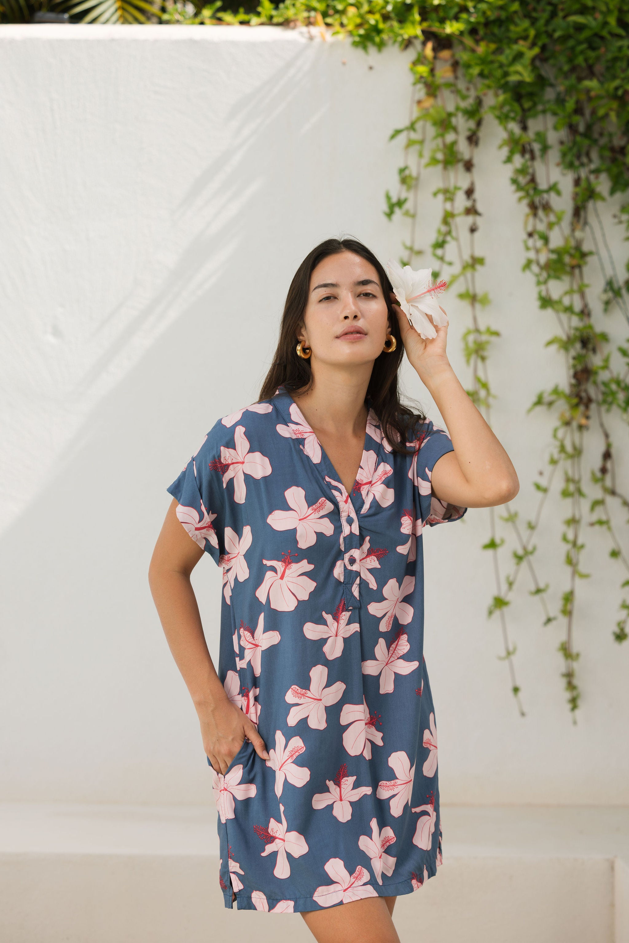 woman with black hair wearing a casual shirt dress with button up v neckline in a navy and pink hibiscus print.