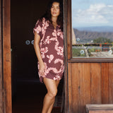 woman with brown hair wearing a brown colored button up v neckline dress with light pink lei awapuhi pattern