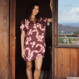 woman with brown hair wearing a brown colored button up v neckline dress with light pink lei awapuhi pattern