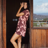 woman with brown hair wearing a brown colored button up v neckline dress with light pink lei awapuhi pattern