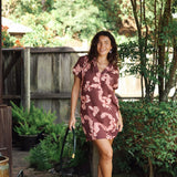 woman with brown hair wearing a brown colored button up v neckline dress with light pink lei awapuhi pattern