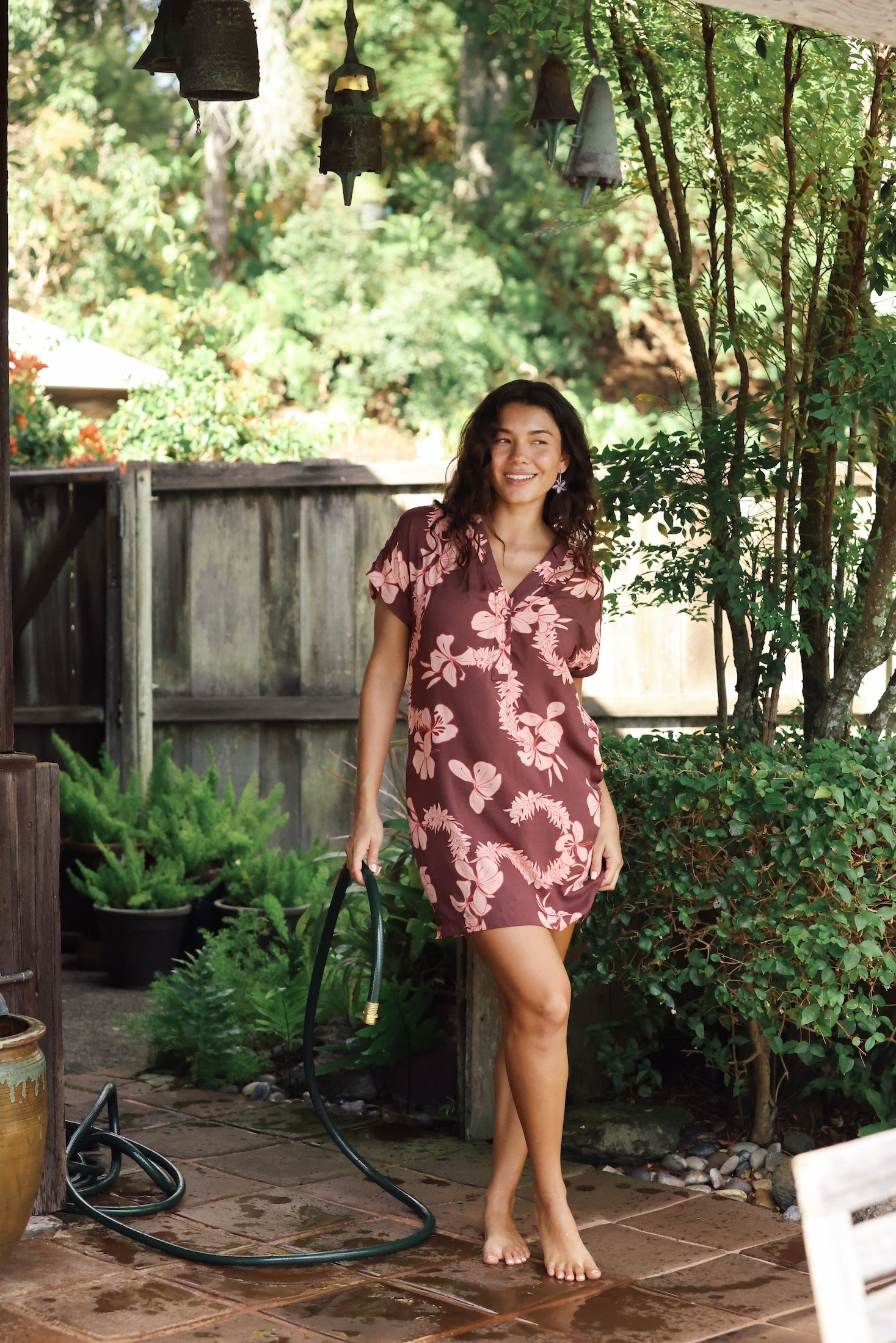 woman with brown hair wearing a brown colored button up v neckline dress with light pink lei awapuhi pattern