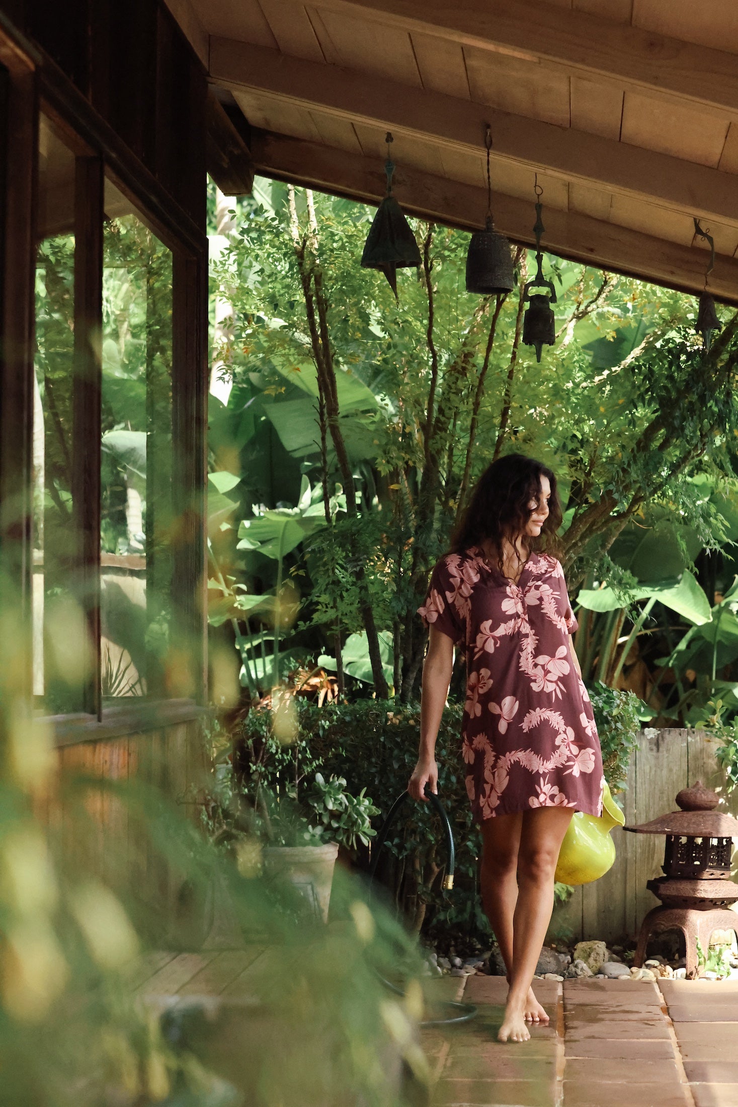 woman with brown hair wearing a brown colored button up v neckline dress with light pink lei awapuhi pattern