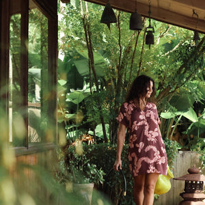 woman with brown hair wearing a brown colored button up v neckline dress with light pink lei awapuhi pattern