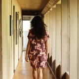 woman with brown hair wearing a brown colored button up v neckline dress with light pink lei awapuhi pattern