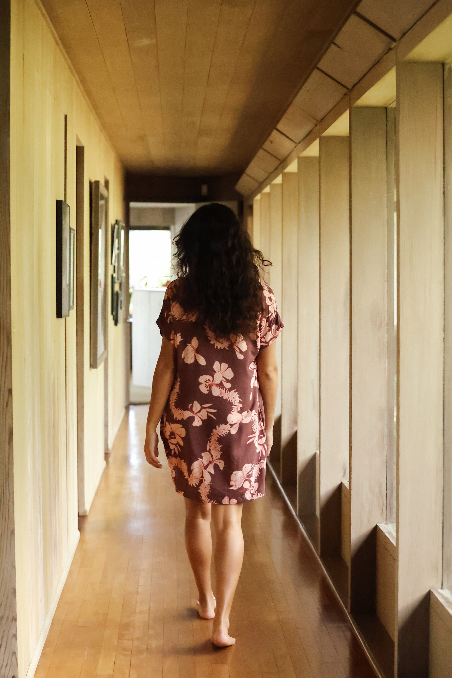 woman with brown hair wearing a brown colored button up v neckline dress with light pink lei awapuhi pattern