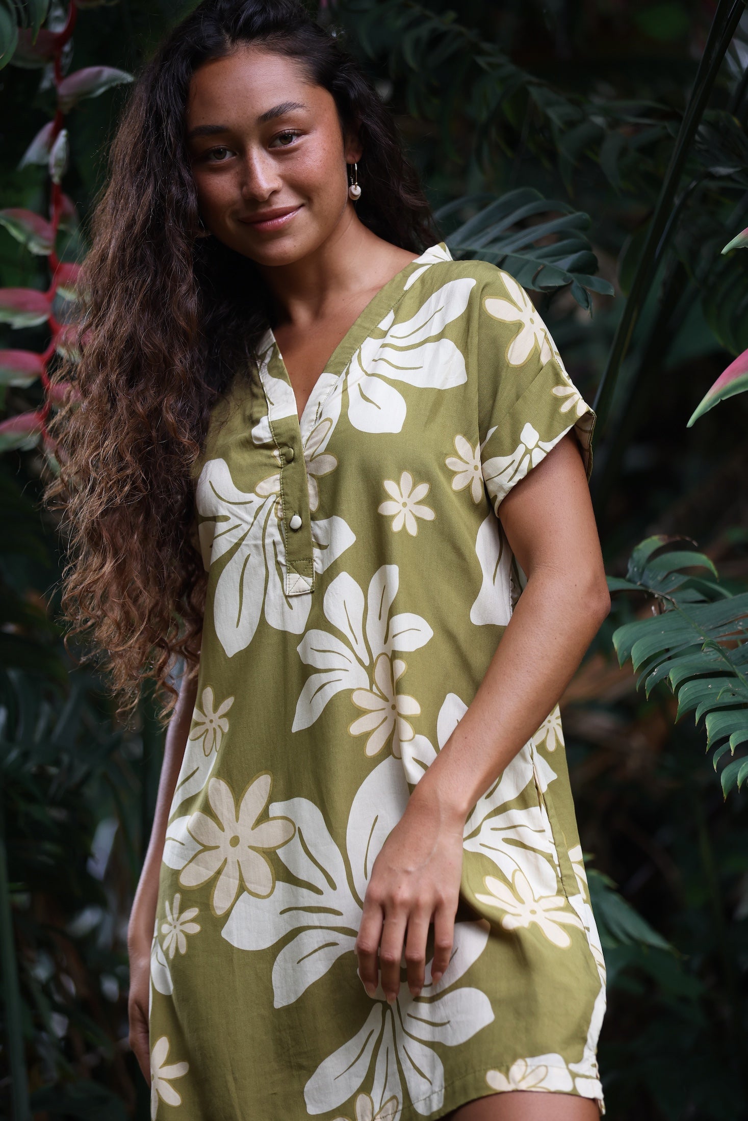 woman with brown hair wearing a shirt dress with v neck in green print with naupaka pattern