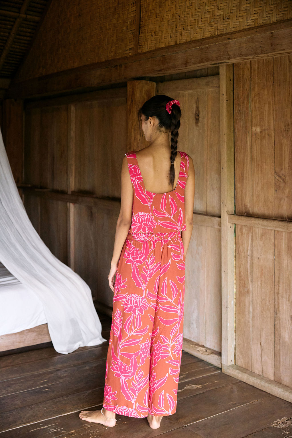A woman with dark hair wears a YIREH flowy cropped top. It is the Naia Top in the Garden 'Awapuhi print.