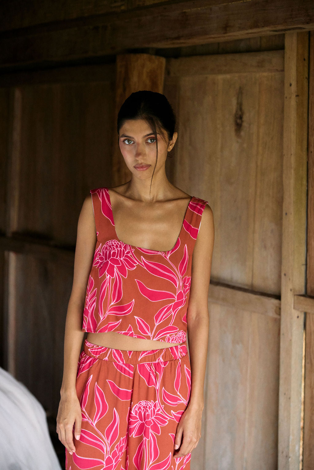 A woman with dark hair wears a YIREH flowy cropped top. It is the Naia Top in the Garden 'Awapuhi print.