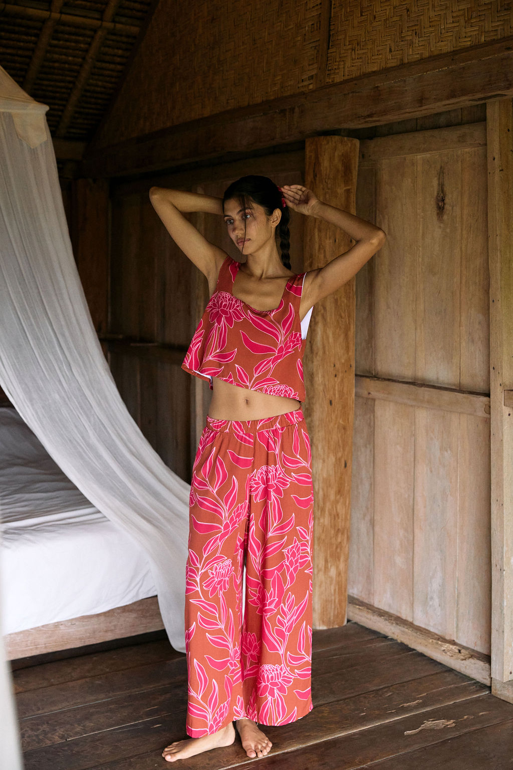 A woman with dark hair wears a YIREH flowy cropped top. It is the Naia Top in the Garden 'Awapuhi print.