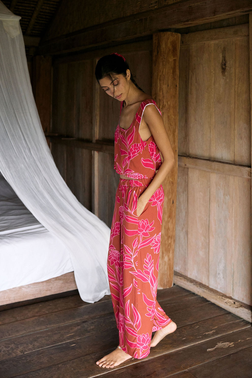 A woman with dark hair wears a YIREH flowy cropped top. It is the Naia Top in the Garden 'Awapuhi print.