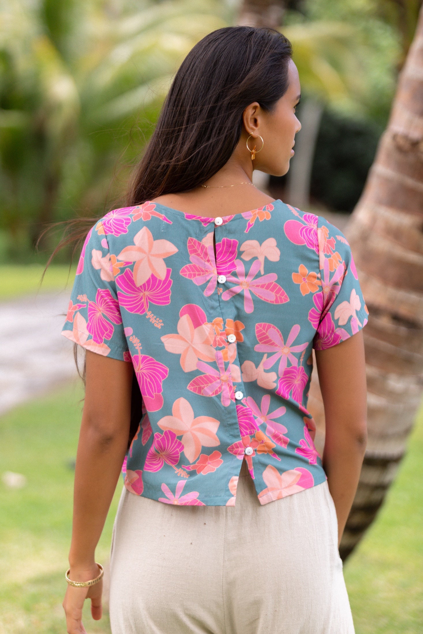 woman with brown hair wearing a teal t-shirt top with orange and pink foral print