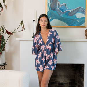 woman with black hair wearing a v neck playsuit with half sleeves in a navy and pink hibiscus print.