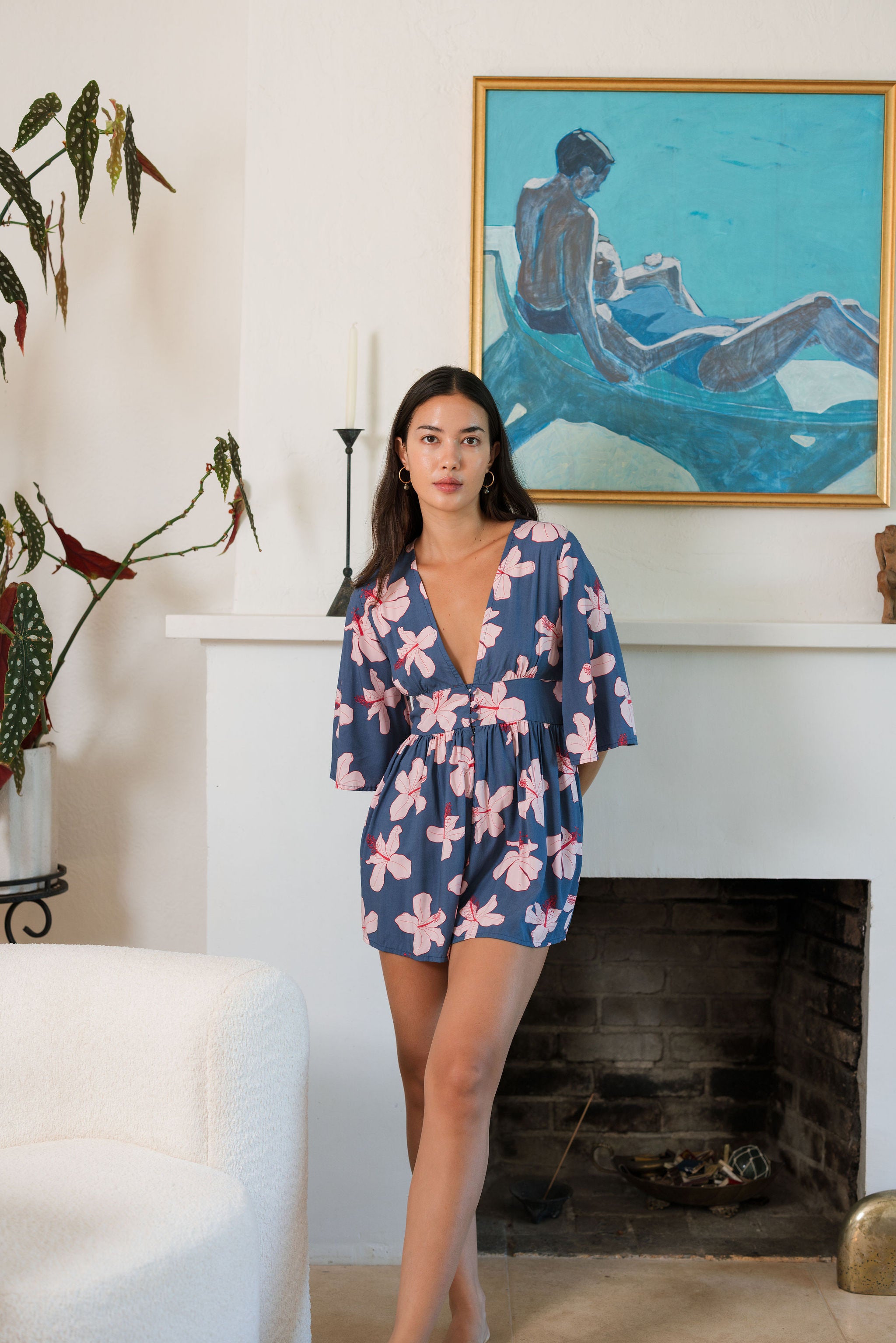 woman with black hair wearing a v neck playsuit with half sleeves in a navy and pink hibiscus print.