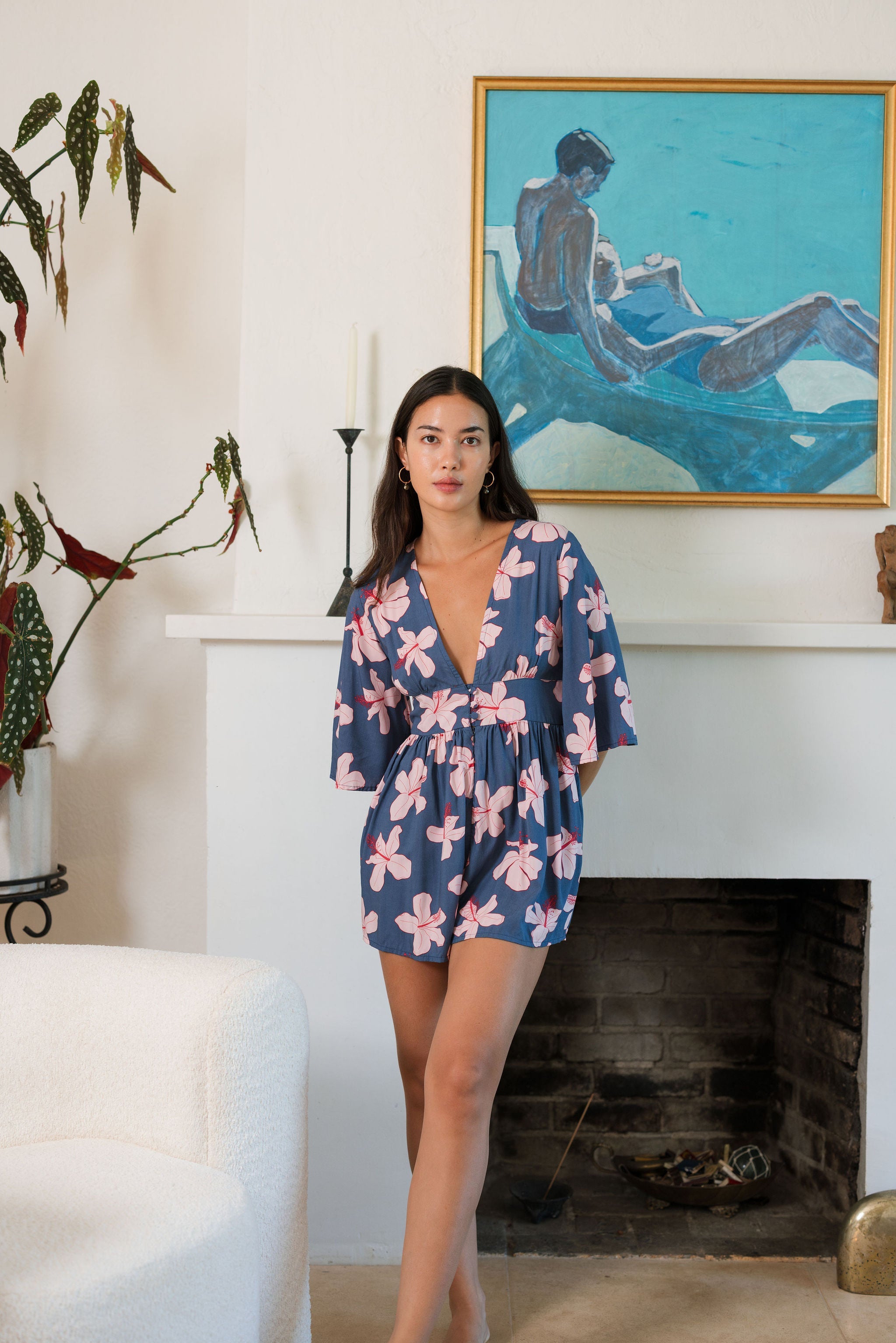 woman with black hair wearing a v neck playsuit with half sleeves in a navy and pink hibiscus print.