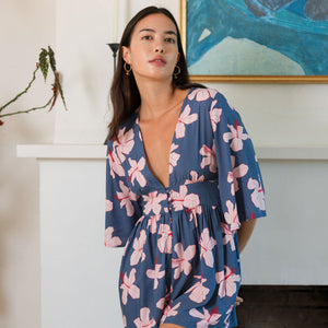 woman with black hair wearing a v neck playsuit with half sleeves in a navy and pink hibiscus print.