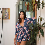 woman with black hair wearing a v neck playsuit with half sleeves in a navy and pink hibiscus print.