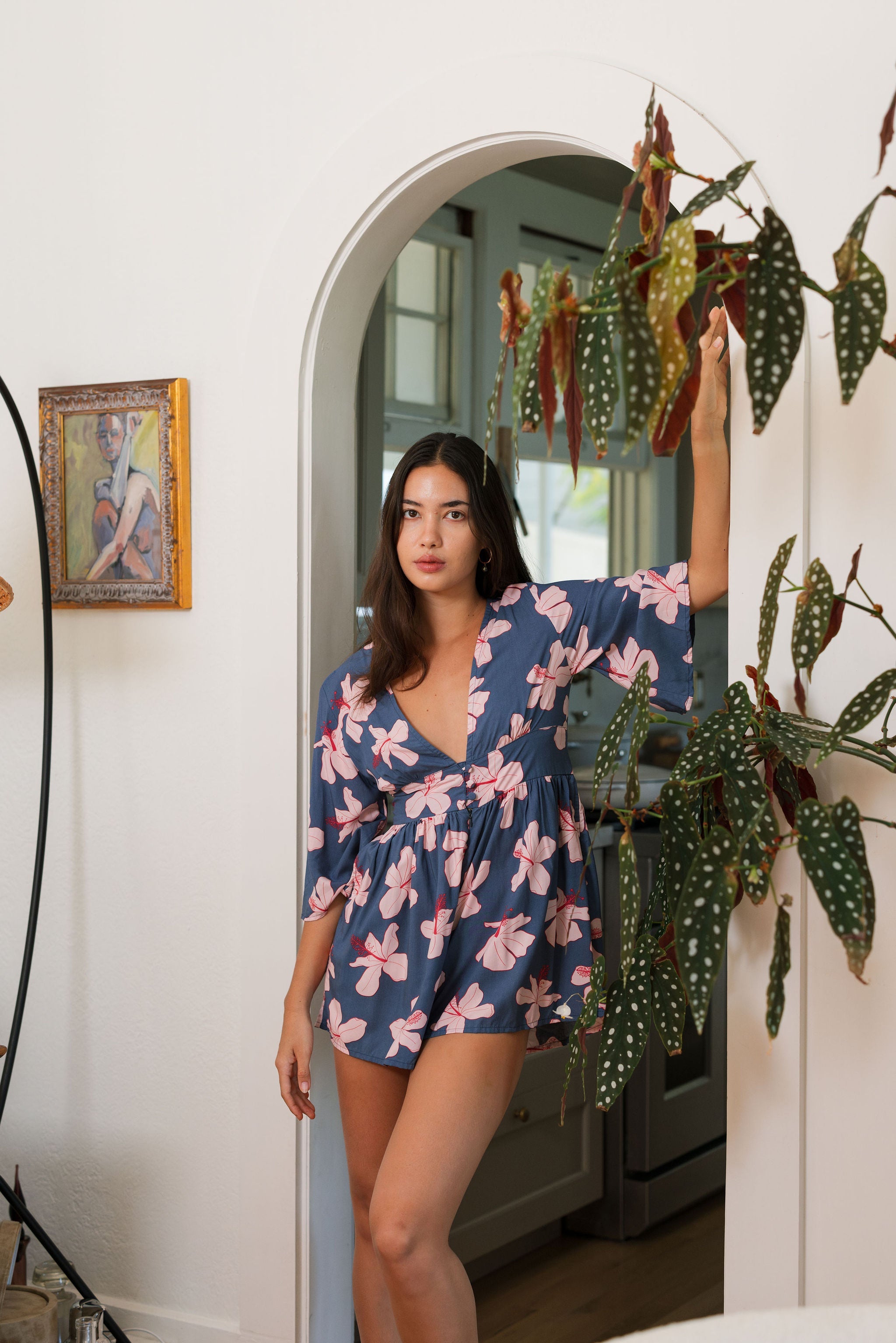 woman with black hair wearing a v neck playsuit with half sleeves in a navy and pink hibiscus print.