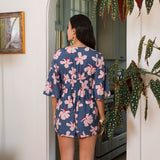 woman with black hair wearing a v neck playsuit with half sleeves in a navy and pink hibiscus print.