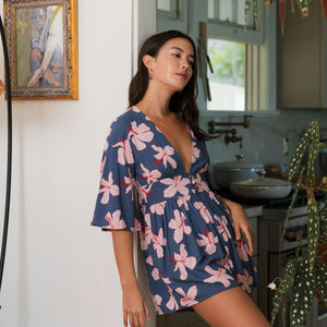 woman with black hair wearing a v neck playsuit with half sleeves in a navy and pink hibiscus print.
