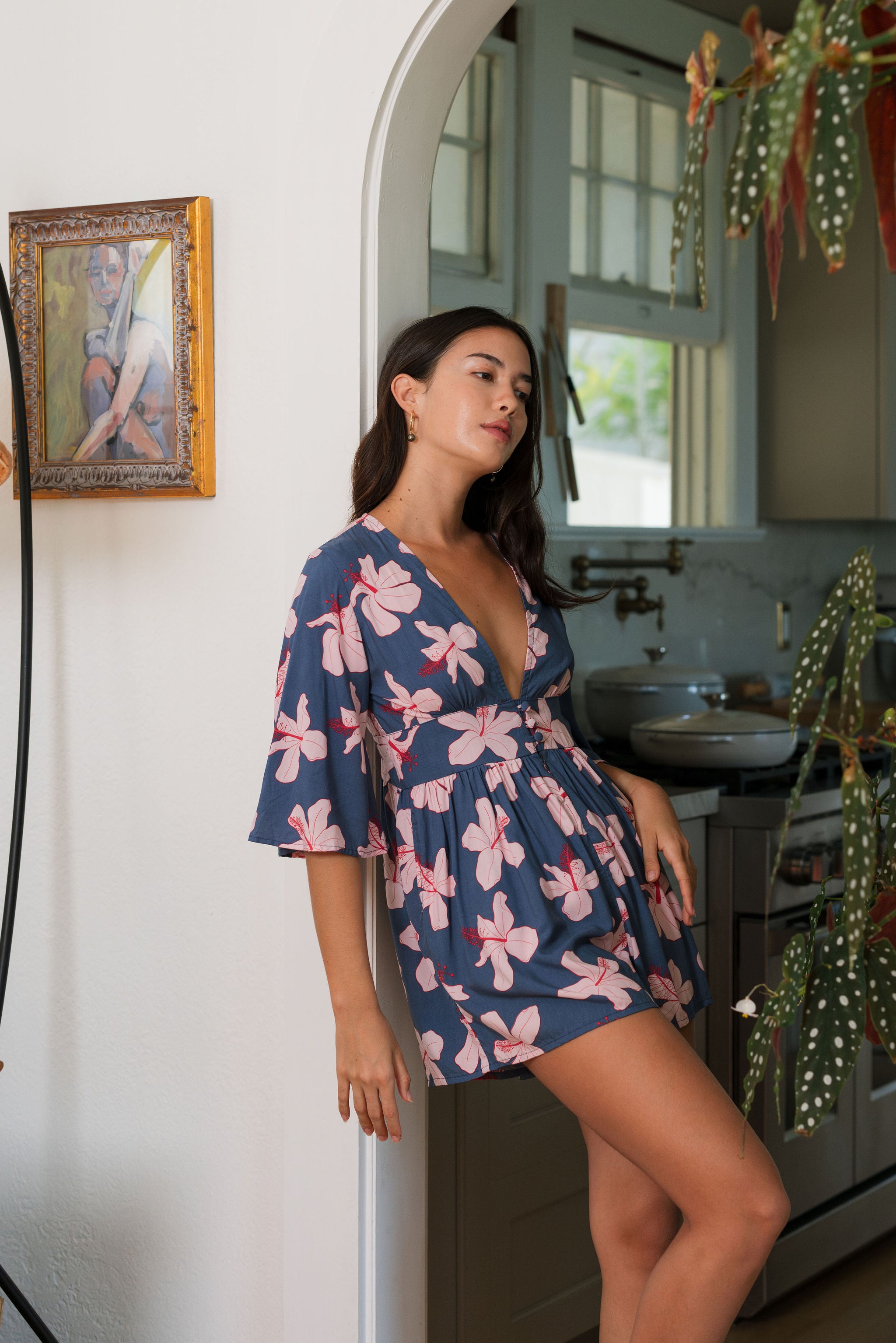 woman with black hair wearing a v neck playsuit with half sleeves in a navy and pink hibiscus print.