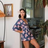 woman with black hair wearing a v neck playsuit with half sleeves in a navy and pink hibiscus print.