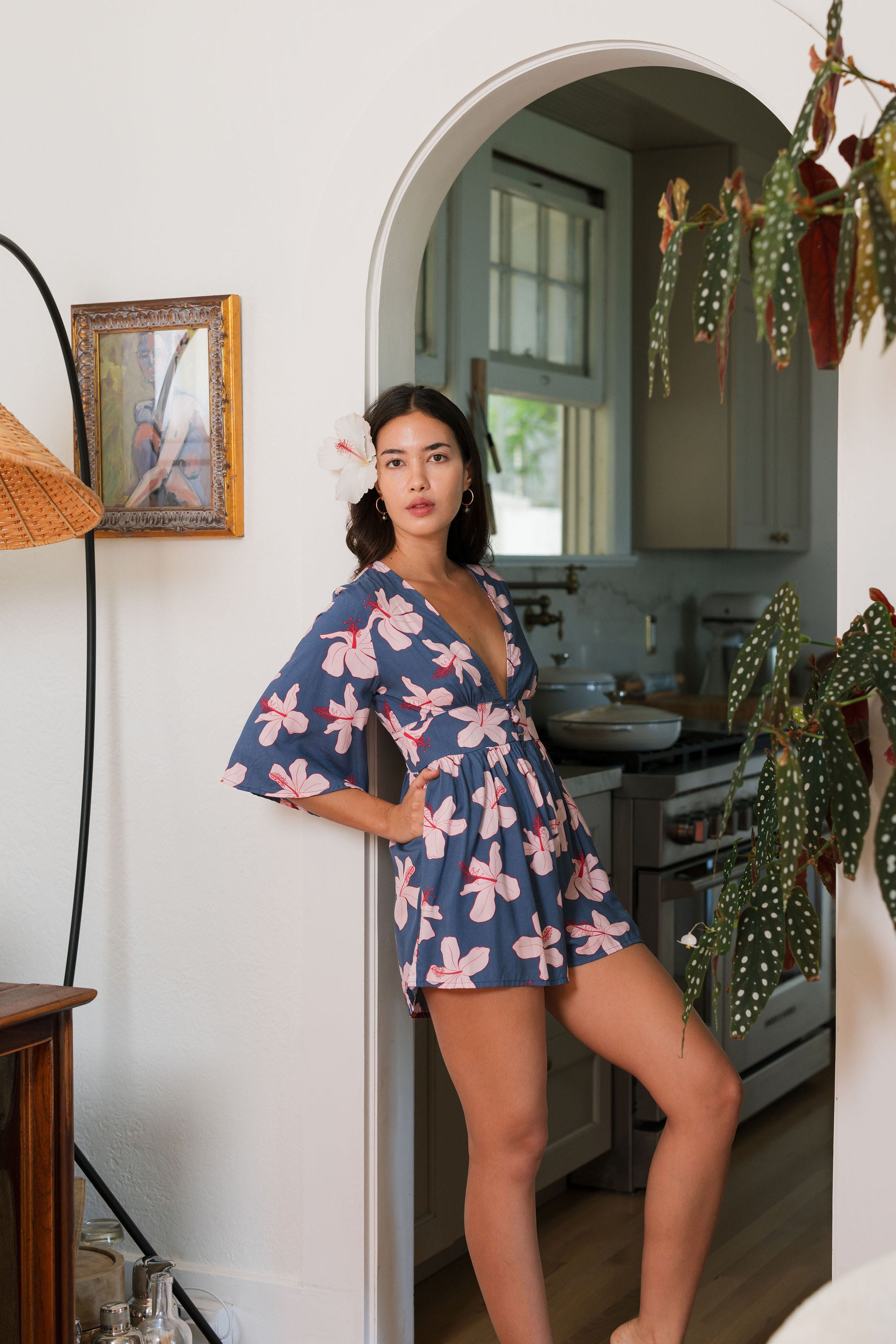 woman with black hair wearing a v neck playsuit with half sleeves in a navy and pink hibiscus print.