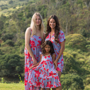 little girl with brown hair wearing a mid length dress with periwinkle background and bright red hibiscus print.