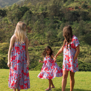 little girl with brown hair wearing a mid length dress with periwinkle background and bright red hibiscus print.