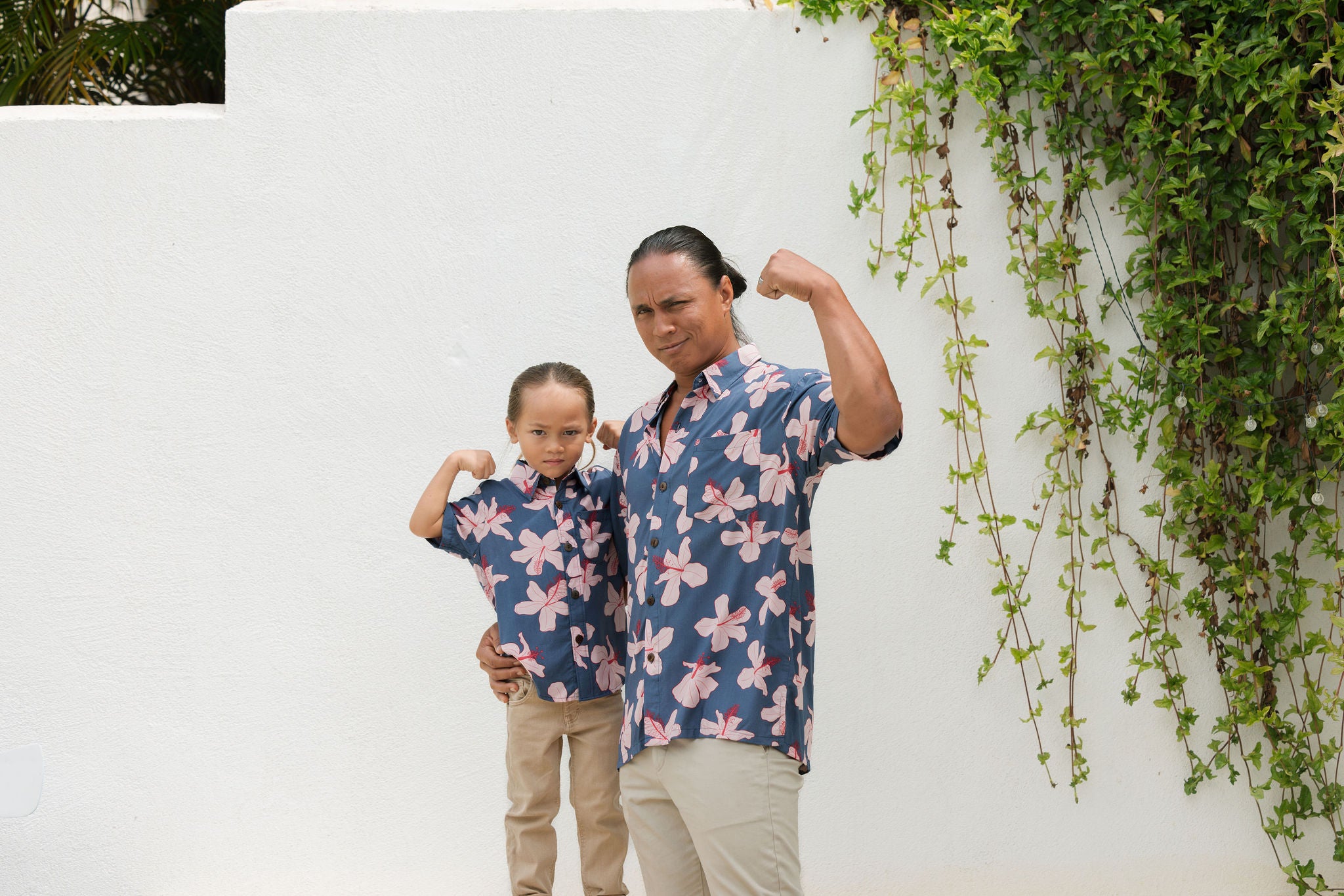 little boy wearing button up aloha shirt in navy and pink hibiscus print.
