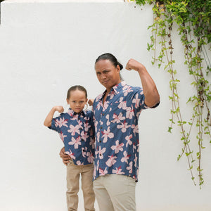 little boy wearing button up aloha shirt in navy and pink hibiscus print.