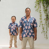 man wearing button up aloha shirt in navy and pink hibiscus print.