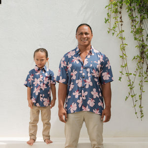 man wearing button up aloha shirt in navy and pink hibiscus print.