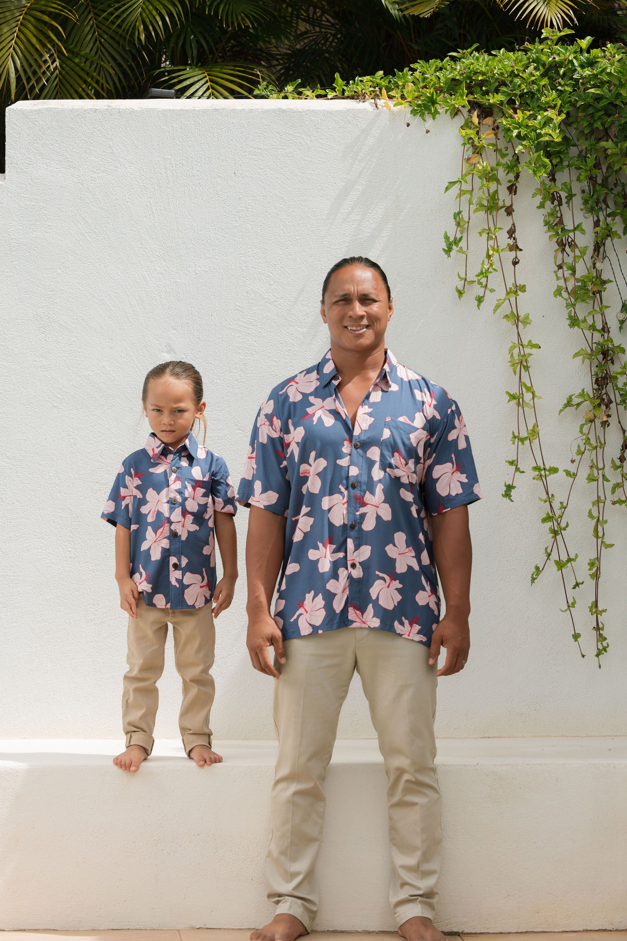 man wearing button up aloha shirt in navy and pink hibiscus print.