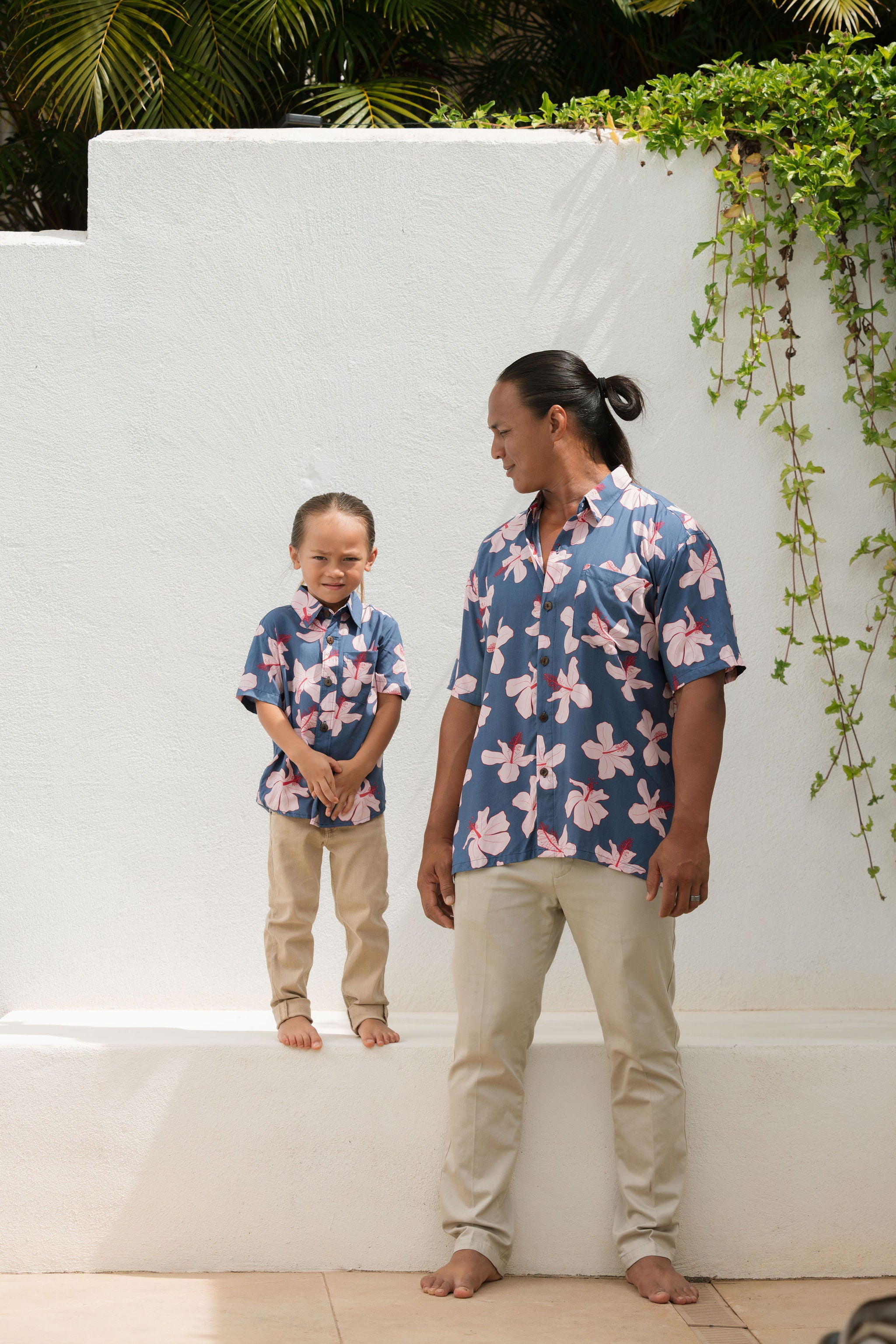 man wearing button up aloha shirt in navy and pink hibiscus print.