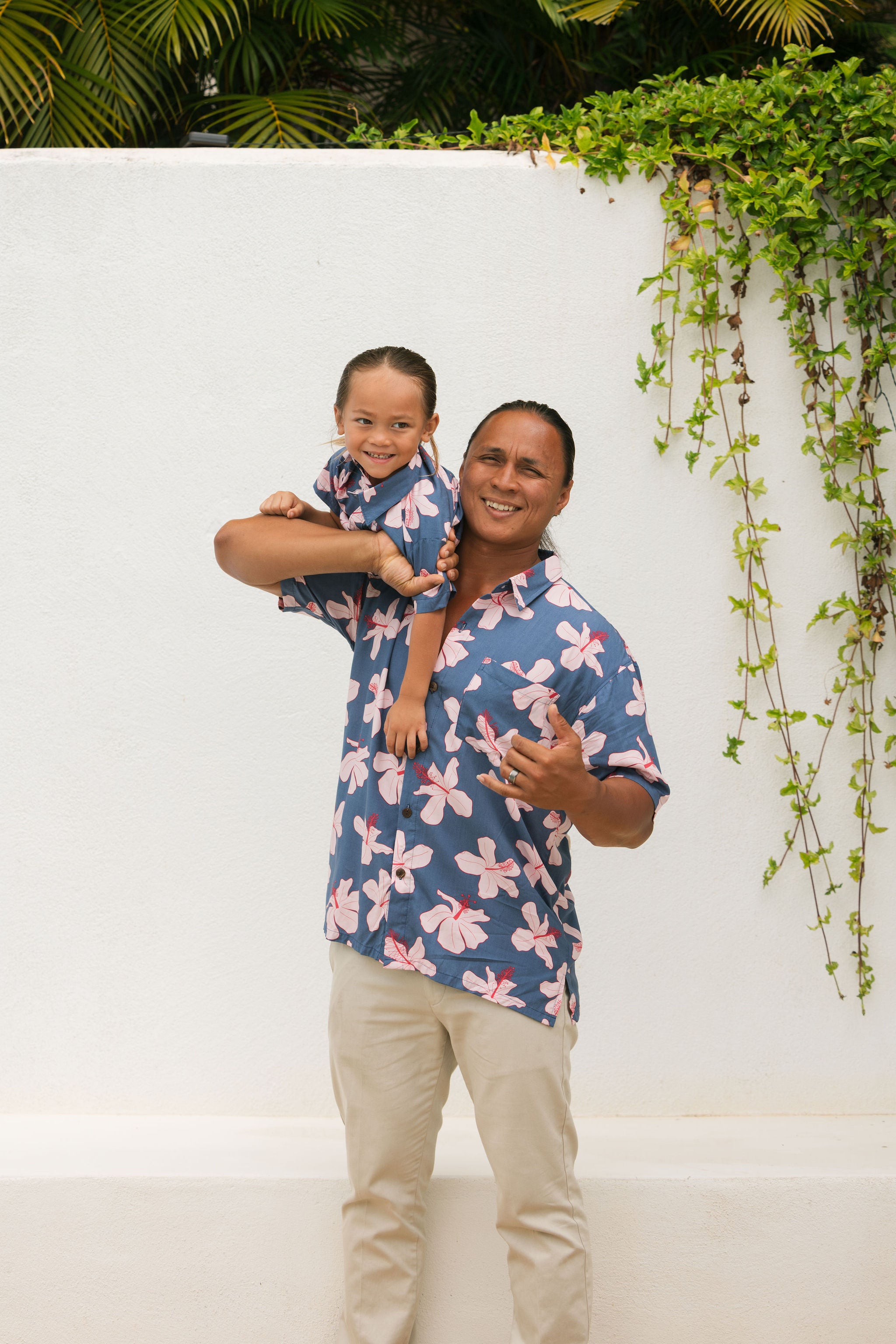 man wearing button up aloha shirt in navy and pink hibiscus print.