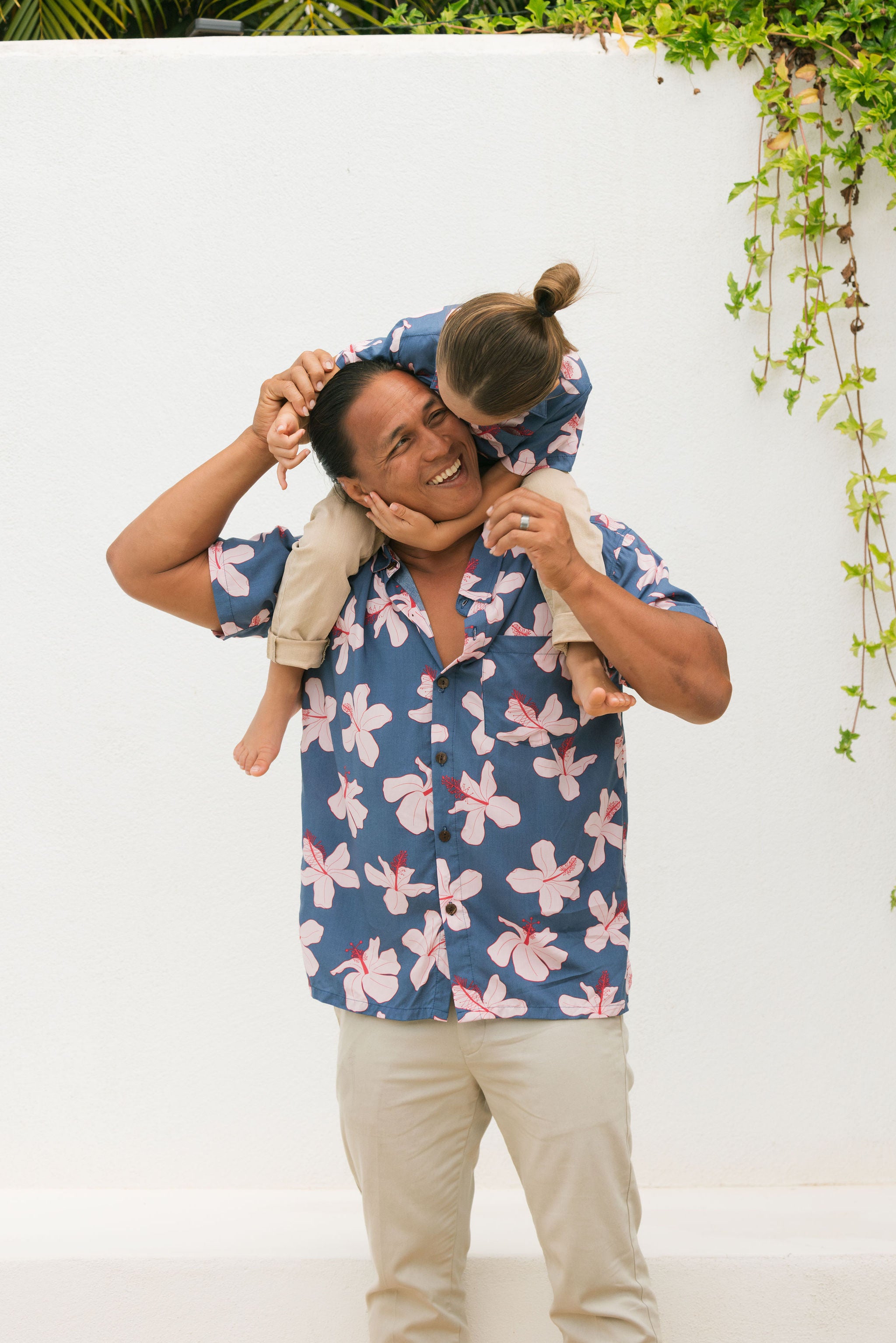 man wearing button up aloha shirt in navy and pink hibiscus print.