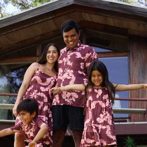 man wearing brown aloha shirt with pink lei awapuhi print