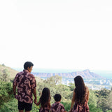 man wearing brown aloha shirt with pink lei awapuhi print