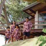 man wearing brown aloha shirt with pink lei awapuhi print