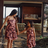 little girl wearing a long brown dress with tie sleeve with light pink lei awapuhi print walking with her mother in matching dress