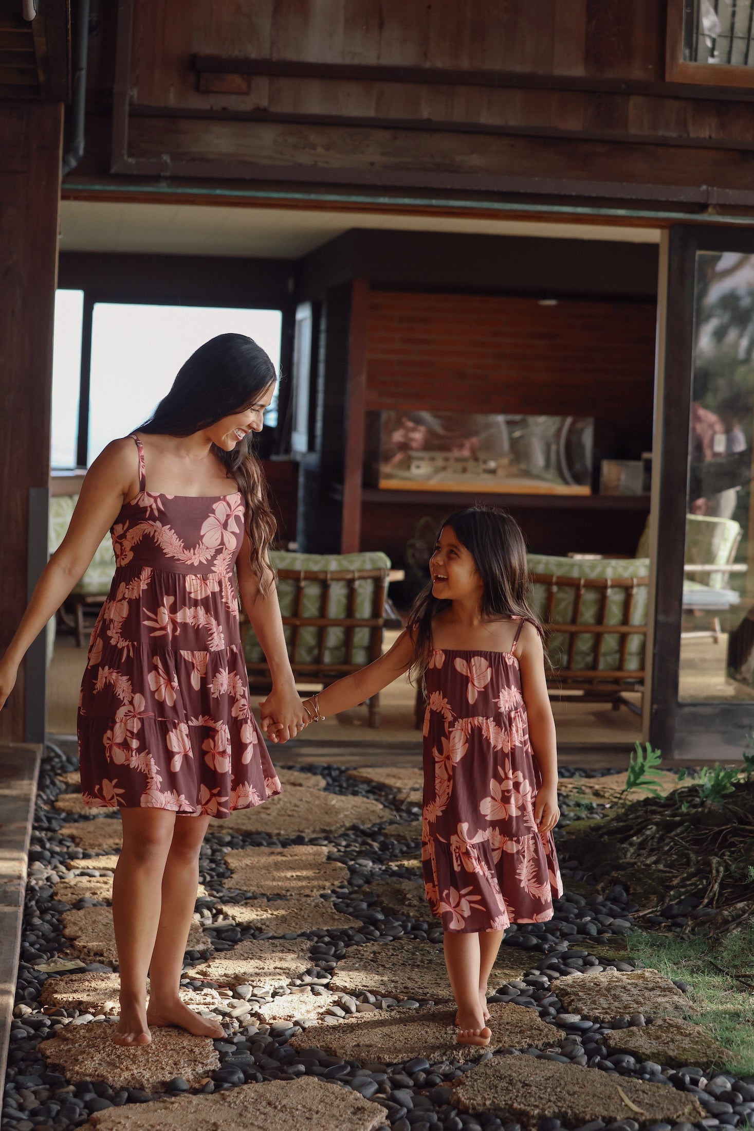 little girl wearing a long brown dress with tie sleeve with light pink lei awapuhi print walking with her mother in matching dress